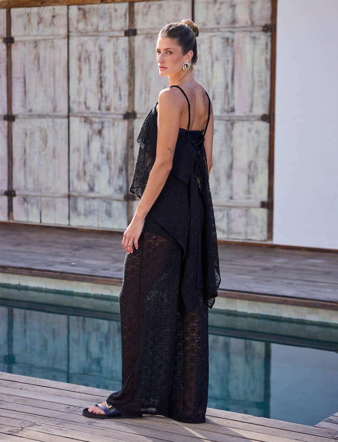 Modelo vestindo blusa preta de renda com transparência e barra assimétrica para look elegante de saída de praia