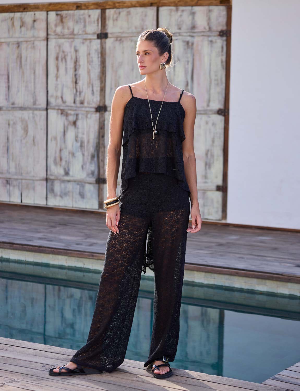 Mulher vestindo calça pantalona preta de renda com short under para composição resort sofisticada