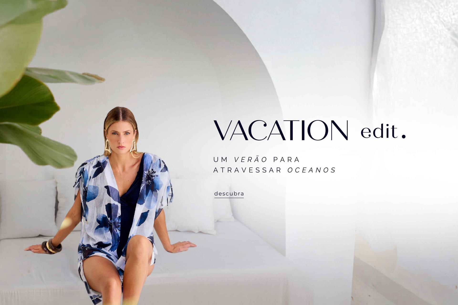 Modelo em cenário mediterrâneo branco usando kimono floral azul sobre maiô marinho