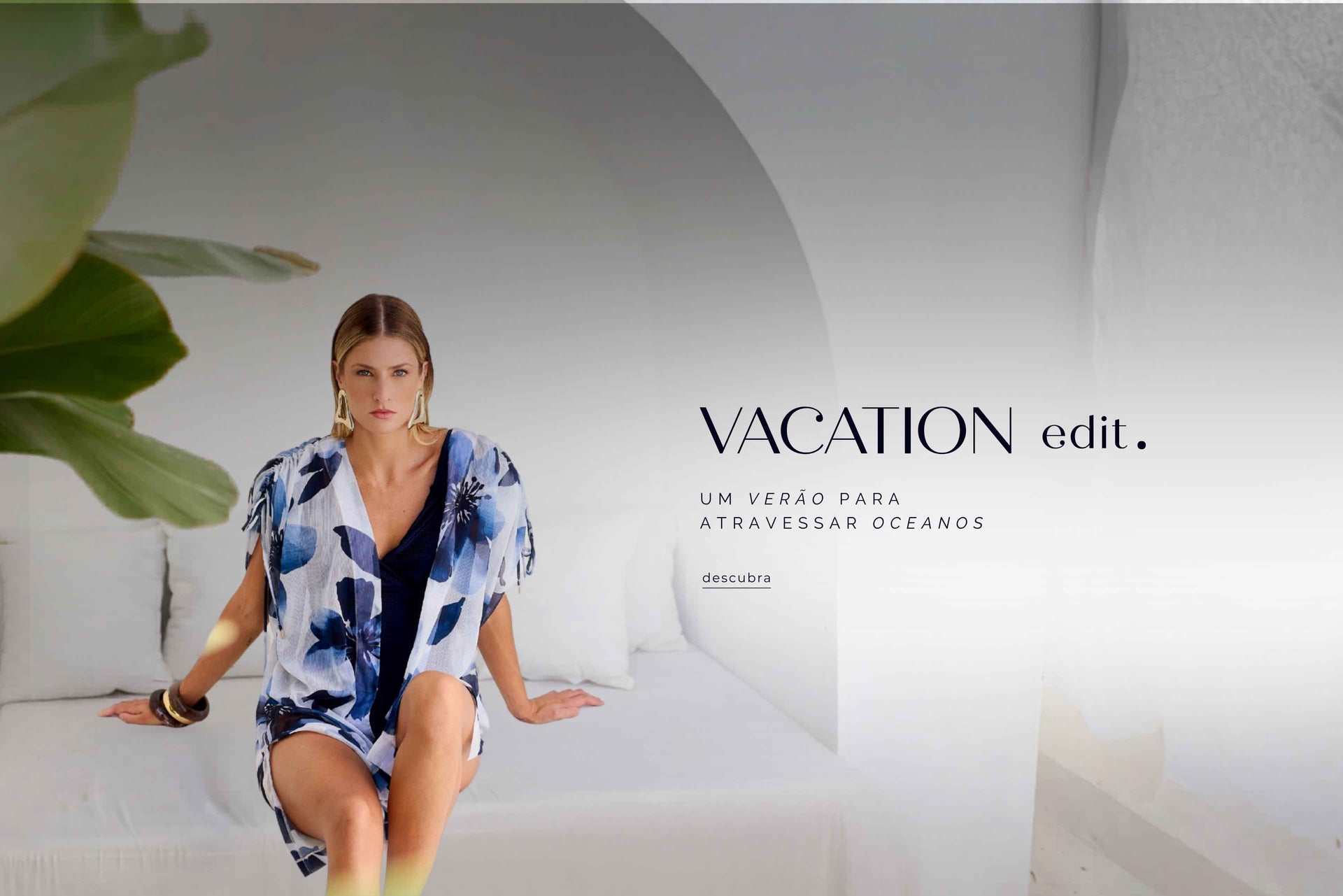 Modelo em cenário mediterrâneo branco usando kimono floral azul sobre maiô marinho