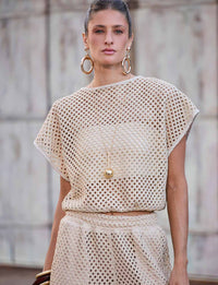 Mulher usando blusa ampla bege de trama vazada com visual de crochê em composição sofisticada de resortwear
