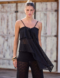 Mulher usando blusa assimétrica preta de renda com leve transparência e top preto em look resort contemporâneo