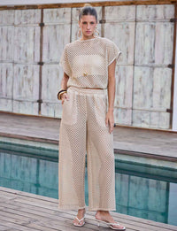 Modelo vestindo blusa bege de trama aberta inspirada no crochê para look elegante de saída de praia