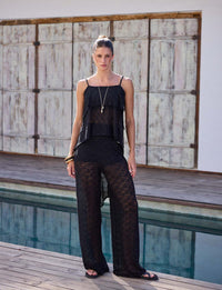 Mulher usando calça flare preta de renda com leve transparência em composição sofisticada de resortwear