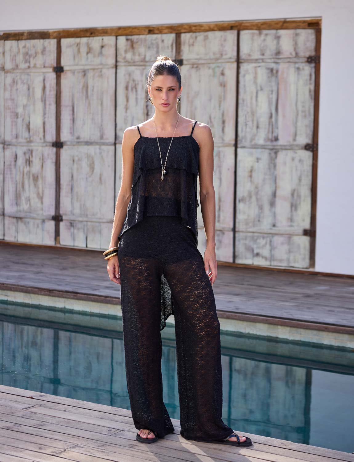 Mulher usando calça flare preta de renda com leve transparência em composição sofisticada de resortwear