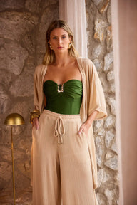 Mulher estilosa com roupa confortável e elegante, usando maiô verde e calças largas em uma decoração rústica com parede de pedra, luxuosa e moderna.