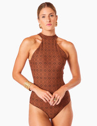 Imagem de mulher com cabelos loiros presos usando maiô halter modelador firenze, acessórios dourados e expressão séria, contra fundo branco.