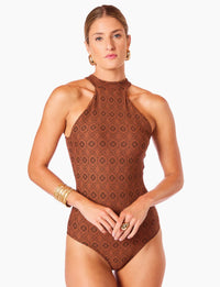 Imagem de mulher com cabelos loiros presos usando maiô halter modelador firenze, acessórios dourados e expressão séria, contra fundo branco.