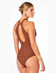 Mulher elegante de perfil usando maiô halter marrom textura firenze com detalhe de abertura nas costas, acessórios dourados e cabelo preso, em fundo branco.