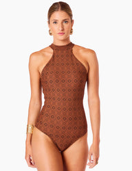 Mulher com cabelo loiro e olhos azuis usando maiô halter modelador com detalhe em hexágonos e círculos, acessório dourado na orelha e pulseira dourada, posando de frente com expressão séria.