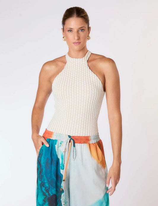 Imagem de mulher usando maiô branco texturizado e calça colorida posando em fundo branco.