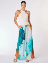 Modelo vestindo maiô texturizado branco e calça pantalona de estampa aquática colorida, posando contra fundo branco.