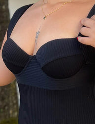 Imagem de uma mulher usando maiô preto com decote, acessório dourado no pescoço e esmalte vermelho nas unhas, refletindo elegância.