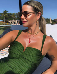 Mulher elegante ao ar livre usando óculos de sol e maiô verde com acessórios de joias, em um dia ensolarado, com fundo de piscina e árvores.