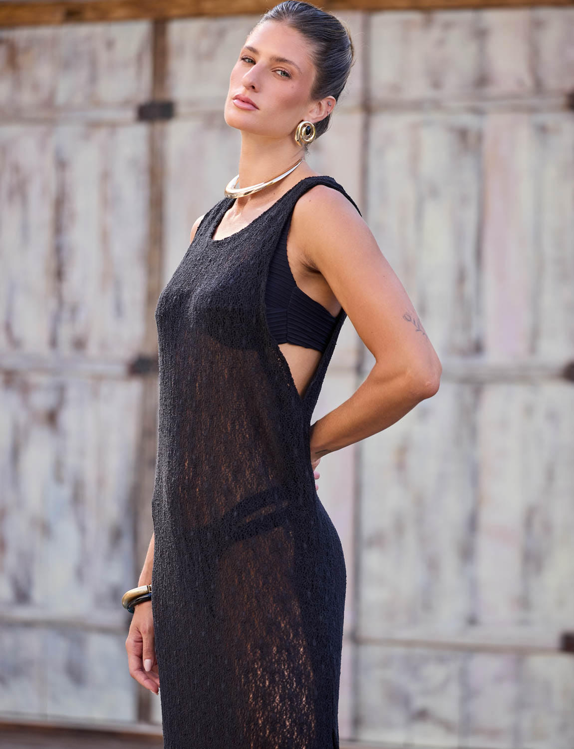 Vista traseira de mulher usando vestido longo de renda preta da Kalini com cinto e fivela banhada a ouro.
